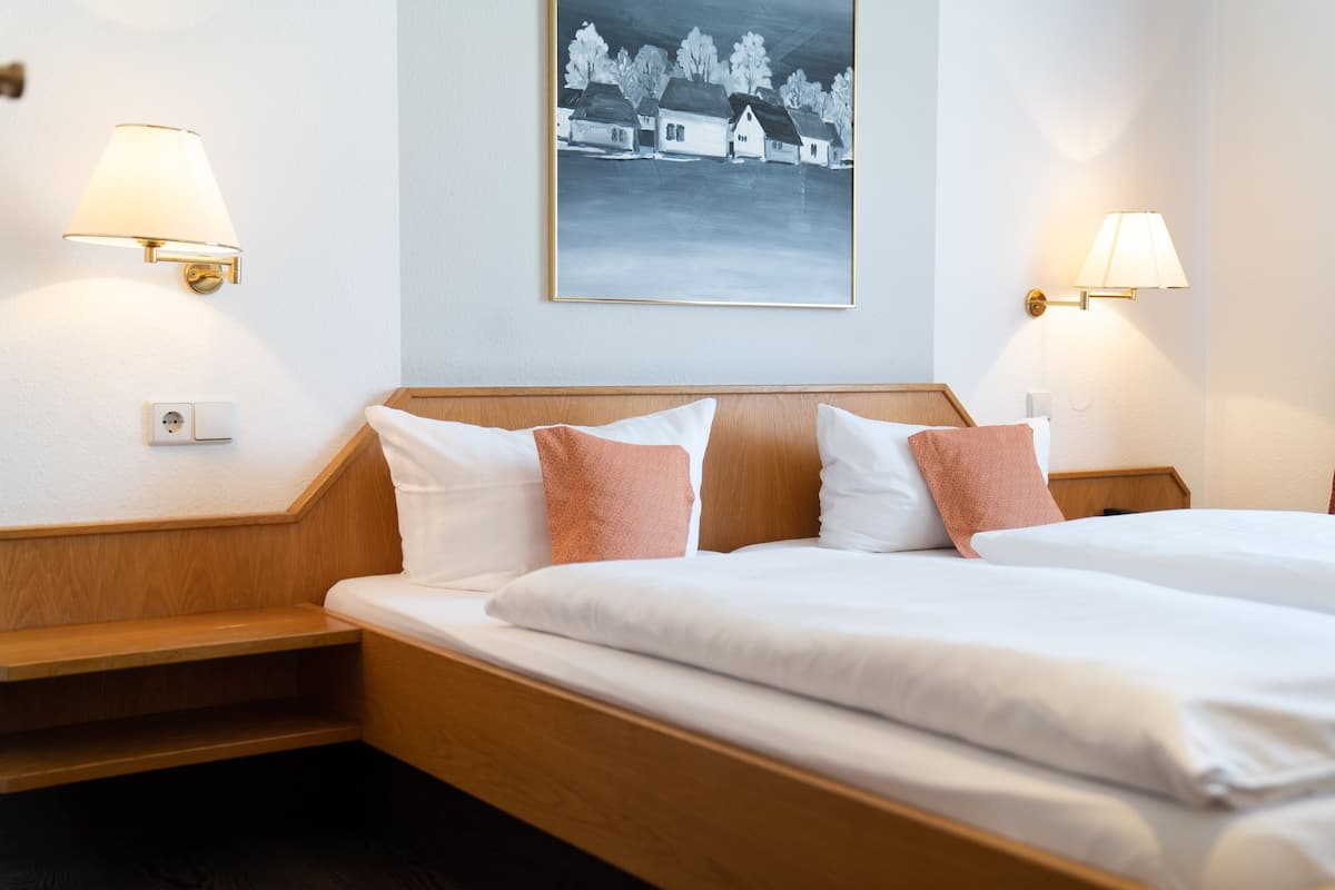 A hotel room with two beds, wooden headboards, white bedding, and two wall-mounted lamps.