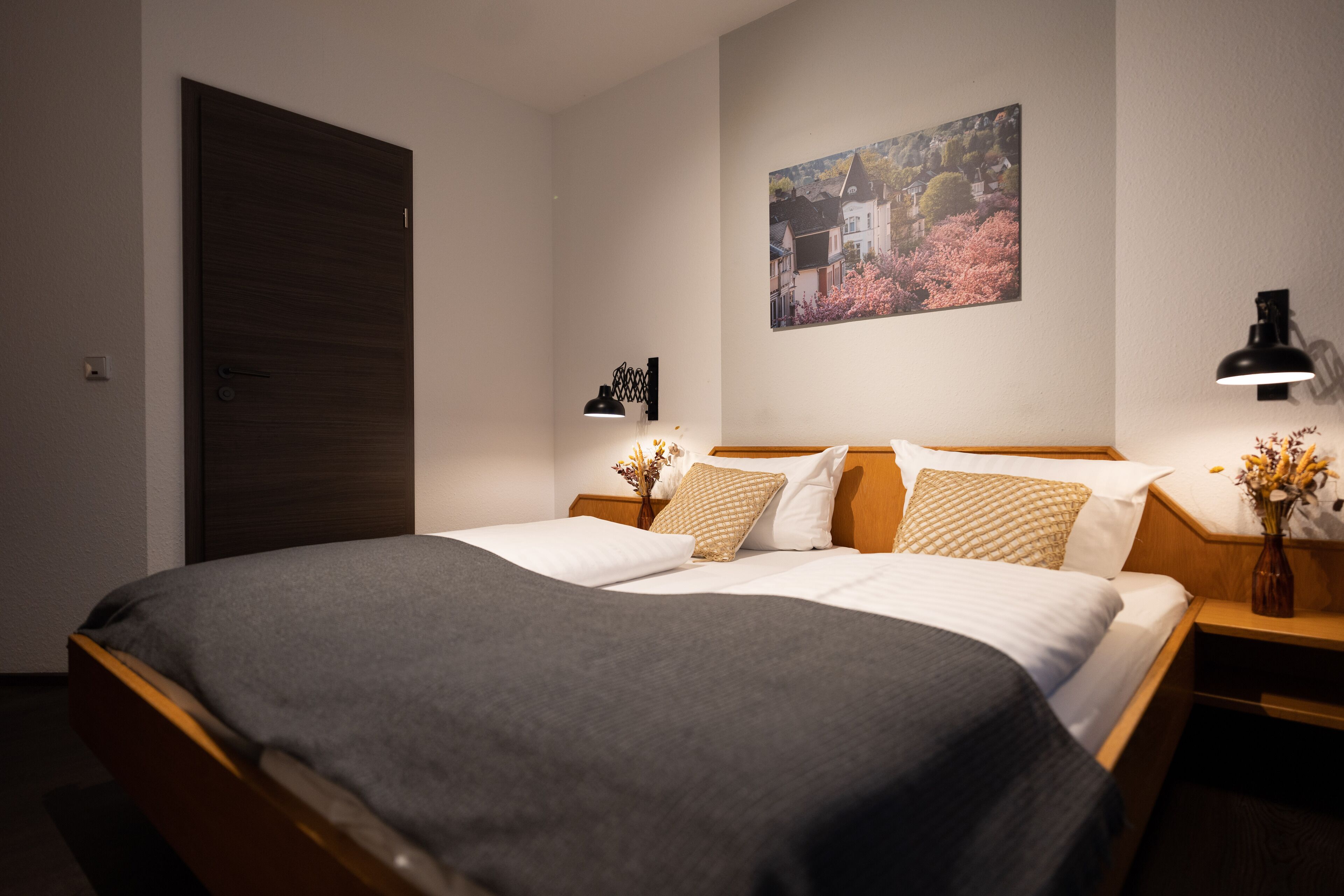 A neatly made bed with a dark blanket, a wooden headboard, and two bedside tables with lamps.