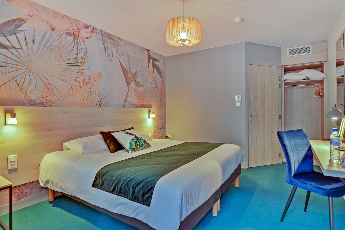 Ein Hotelzimmer mit einem großen Bett, einem blauen Sessel, einem Holzschrank und einer Wandmalerei.