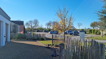 A residential area with a gravel driveway, wooden fence, and parked cars.