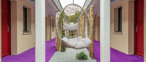 Un pasillo con una silla colgante tipo hamaca, puertas rojas y alfombra morada.