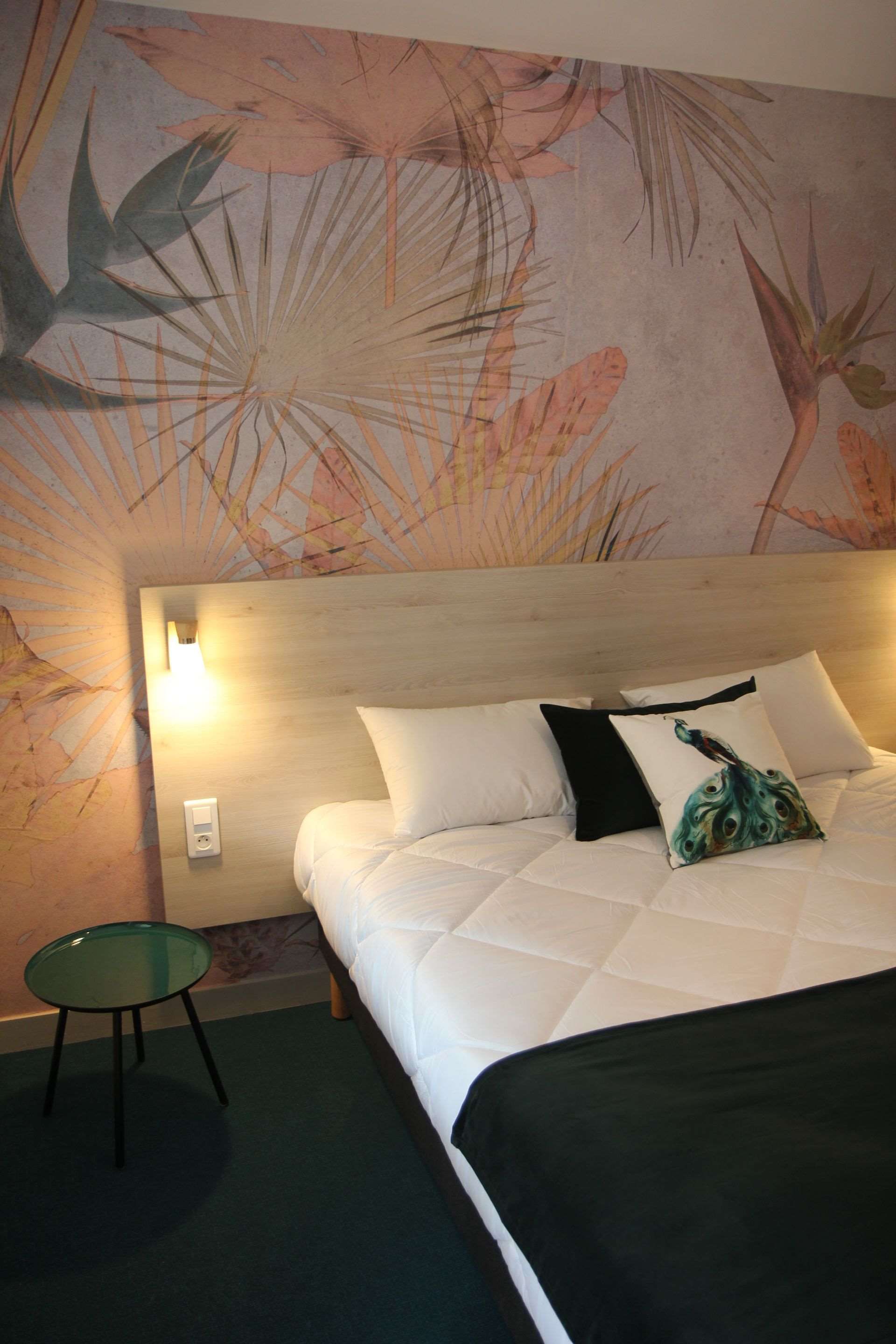 A hotel room with a bed, a bedside table, and a wall with a floral mural.