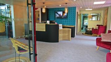 A reception area with a wooden desk, a television mounted on the wall, and a seating area with red chairs.