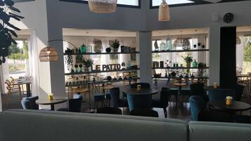 Un café moderno con varias zonas de estar, incluidas mesas y sillas, y una barra con estanterías que exhiben diversos artículos.