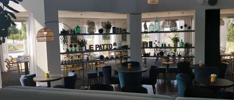 Un café moderno con varias zonas de estar, incluidas mesas y sillas, y una barra con estanterías que exhiben diversos artículos.