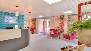 A reception area with a modern desk, red chairs, a large screen, and a decorative wall. - Brit Hotel Au Pays de Vitre (Etrelles)