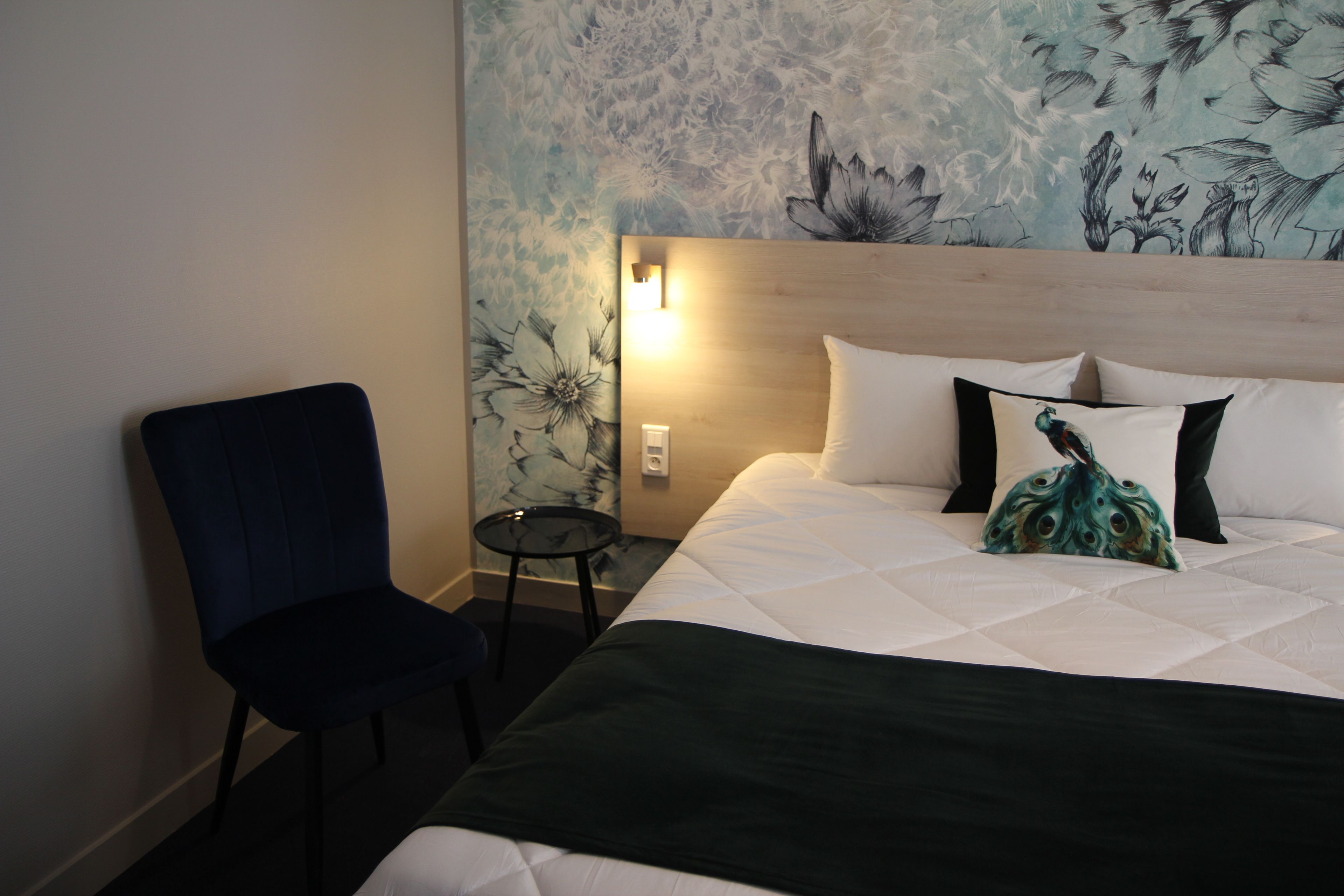 Una habitación de hotel con cama, una silla, una mesita y un mural floral en la pared.