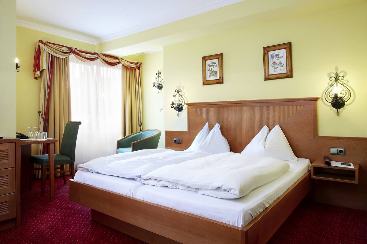 A hotel room with a large bed, a desk with a chair, a dresser, and two wall-mounted lamps.