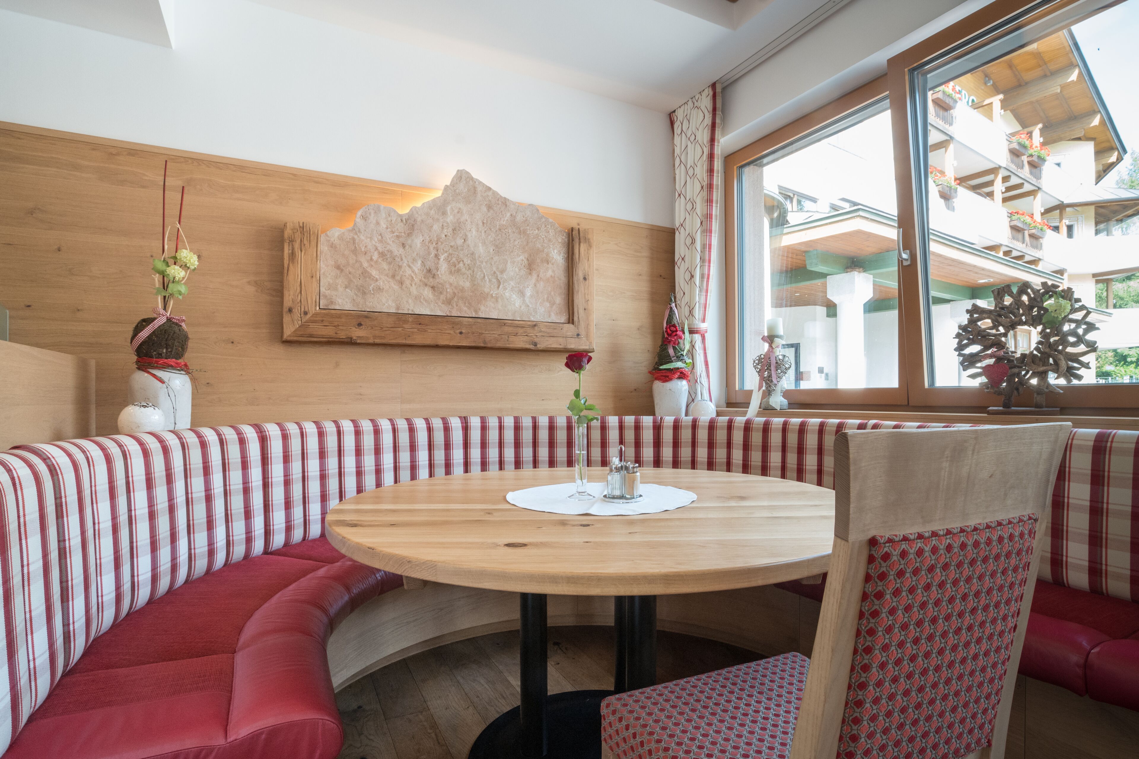 Ein gemütlicher Sitzbereich mit einem runden Holztisch, gestreiften roten und weißen Kissen und einer Holzwand mit einem gerahmten Kunstwerk.