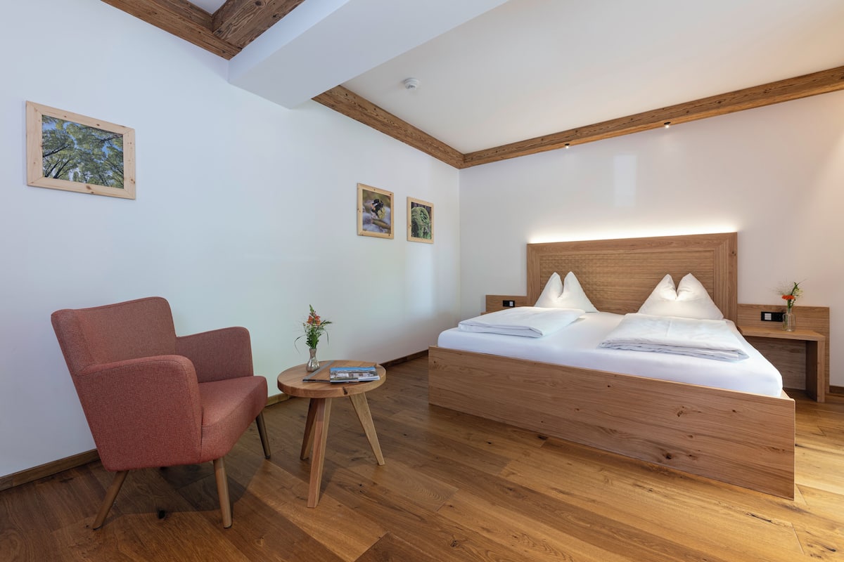 A modern bedroom with a wooden bed, a red armchair, and a small round table with a vase.