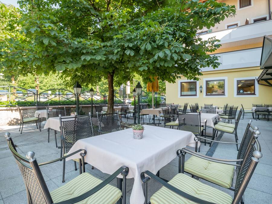 An outdoor patio with tables and chairs, surrounded by greenery and a building.
