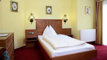 A hotel room with a wooden bed, two bedside tables, a nightstand, a red carpet, and wall-mounted light fixtures.