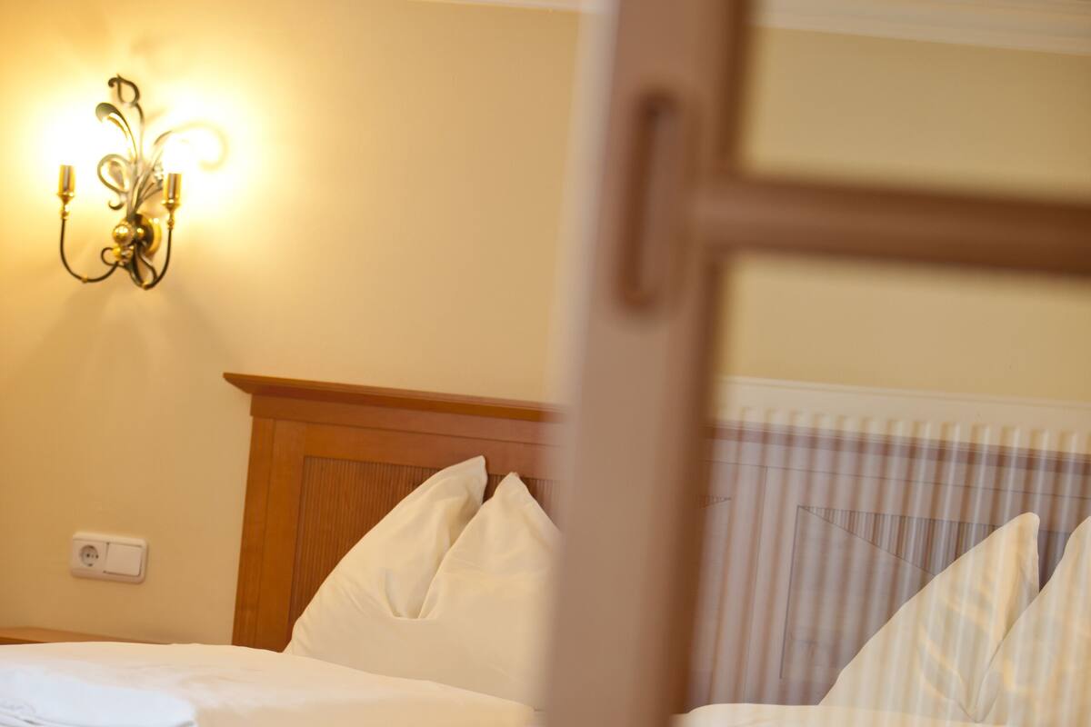 A hotel room with a wooden headboard, a bed with white bedding, and a wall-mounted light fixture.