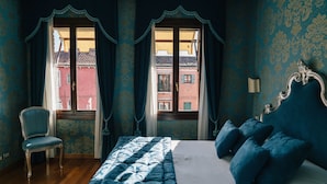 Un dormitorio con cama, una silla y dos ventanas con cortinas.