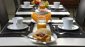 Una mesa de desayuno con tostadas, mermelada y jugo de naranja, junto con tazas y un frutero.