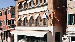 Un edificio histórico con una tienda en la planta baja y apartamentos residenciales en los pisos superiores, junto a un canal con una embarcación amarrada.
