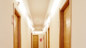 A long, narrow hallway with wooden doors on both sides, a wooden floor, and recessed lighting. - Mapoula (Santiago de Compostela)