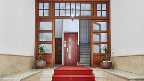 A grand entrance with a red carpet leading to a wooden door with glass panels. - Mapoula (Santiago de Compostela)