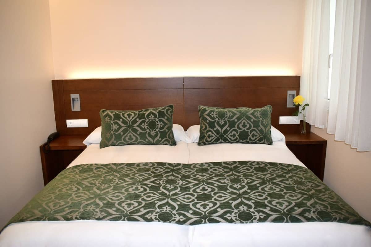 Una habitación de hotel con una cama grande, dos mesitas de noche, un cabecero de madera y una mesita con un jarrón de flores.