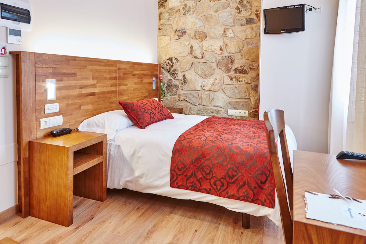 Habitación de hotel con cabecera de madera, pared de acento de piedra, televisión de pantalla plana, mesita de noche de madera y escritorio con control remoto.