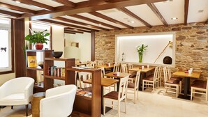 A cozy restaurant with wooden tables and chairs, a stone wall, and a bookshelf with books and a potted plant. - Mapoula (Santiago de Compostela)