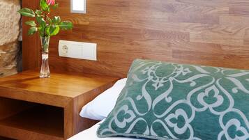 Una mesita de noche de madera con un florero y un cojín estampado verde sobre una cama.
