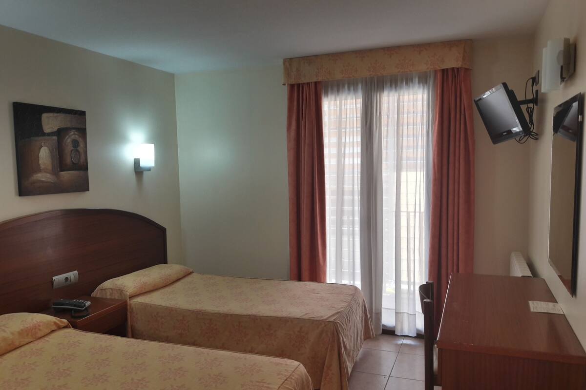 A hotel room with two beds, a desk, a TV, and a painting on the wall.