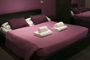 A hotel room with a large bed, purple bedding, and two neatly folded white towels on the bed. - Vatican City Guest House (Rome)