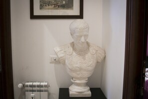 A bust sculpture on a pedestal in a room with a framed picture on the wall and a radiator on the floor. - Vatican City Guest House (Rome)