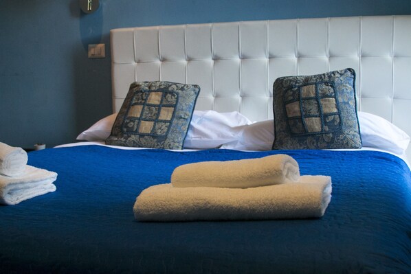 A neatly made bed with blue bedding and two decorative pillows, a white headboard, and a stack of white towels. - Vatican City Guest House (Rome)