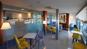 Un moderno vestíbulo de hotel con paredes de vidrio, sillas amarillas y grises, y mesas.