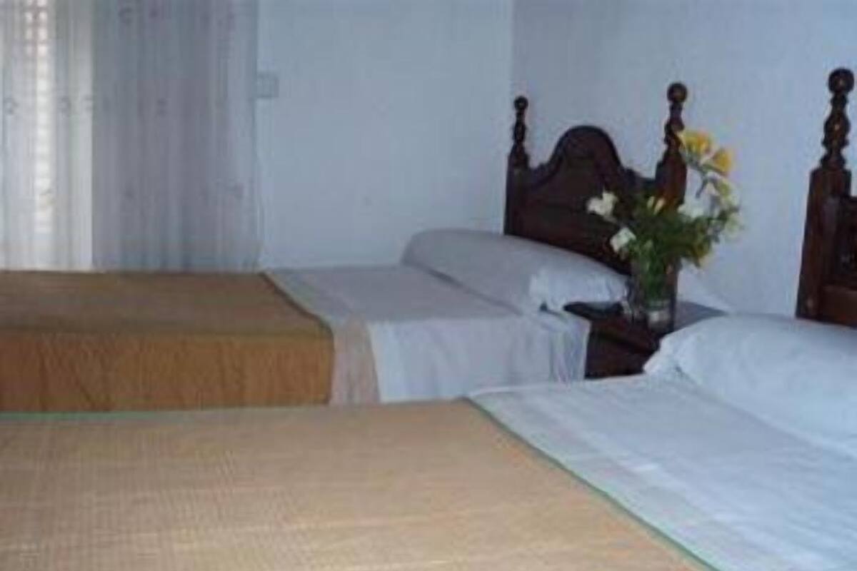 Ein Zimmer mit zwei Betten, einem Nachttisch mit Blumenvase und einem Fenster mit Vorhängen.