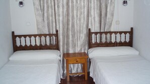 A room with two wooden beds, each with a white bedspread and a wooden nightstand. There are two wall-mounted lamps on either side of the beds. - Castilla (Madrid)