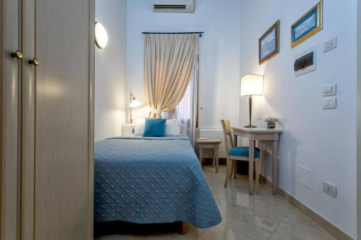 A bedroom with a bed, a chair, a desk, a lamp, and a curtain.