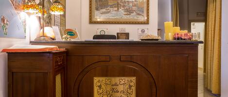 A reception desk with a framed painting, a lit lamp, and a plaque.