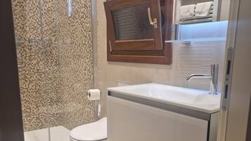 A modern bathroom with a glass shower enclosure, a white toilet, a sink with a mirror, and a towel rack.