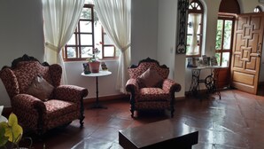 Una habitación con dos sillones decorados, una mesita con una planta en maceta, una máquina de coser y una puerta de madera que dice 'SALIDA'.