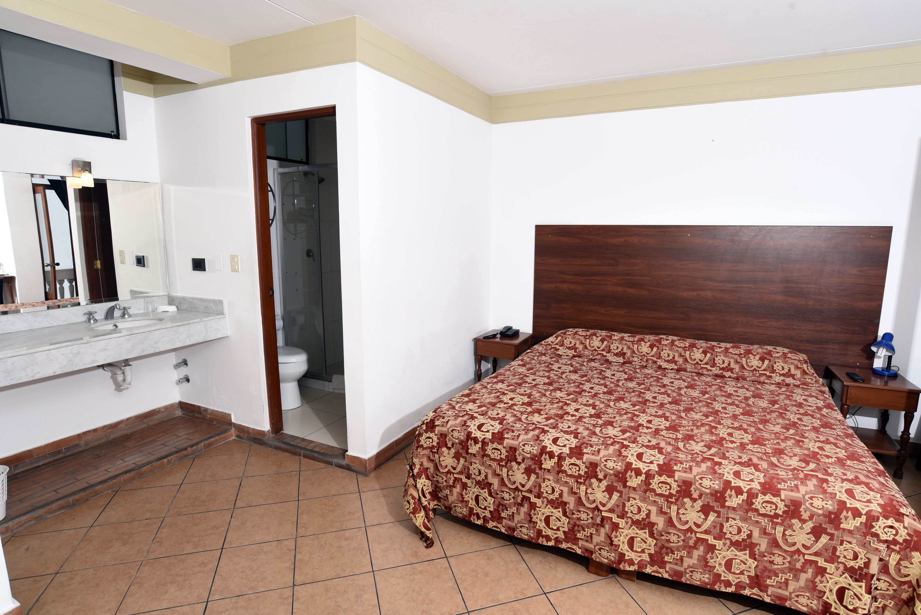A hotel room with a bed, a bathroom with a sink and mirror, and a wooden headboard.