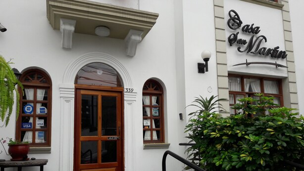 Fachada de edificio con puerta de madera, un cartel que dice "Casa San Martin" y felpudo con la palabra BIENVENIDO.