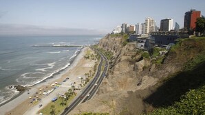 Un paisaje costero con playa, una carretera serpenteando por el acantilado y edificios altos al fondo.