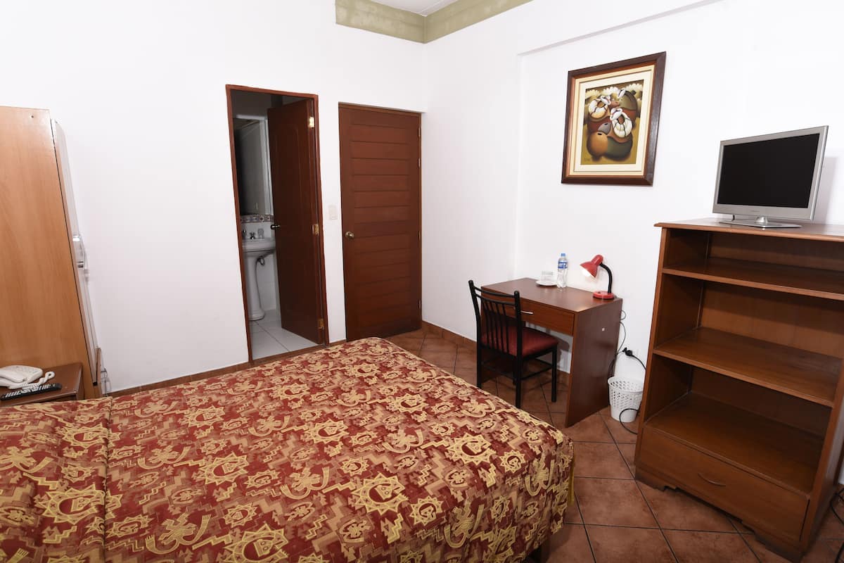Um quarto com uma cama, uma escrivaninha, uma cadeira, uma televisão e um guarda-roupa.