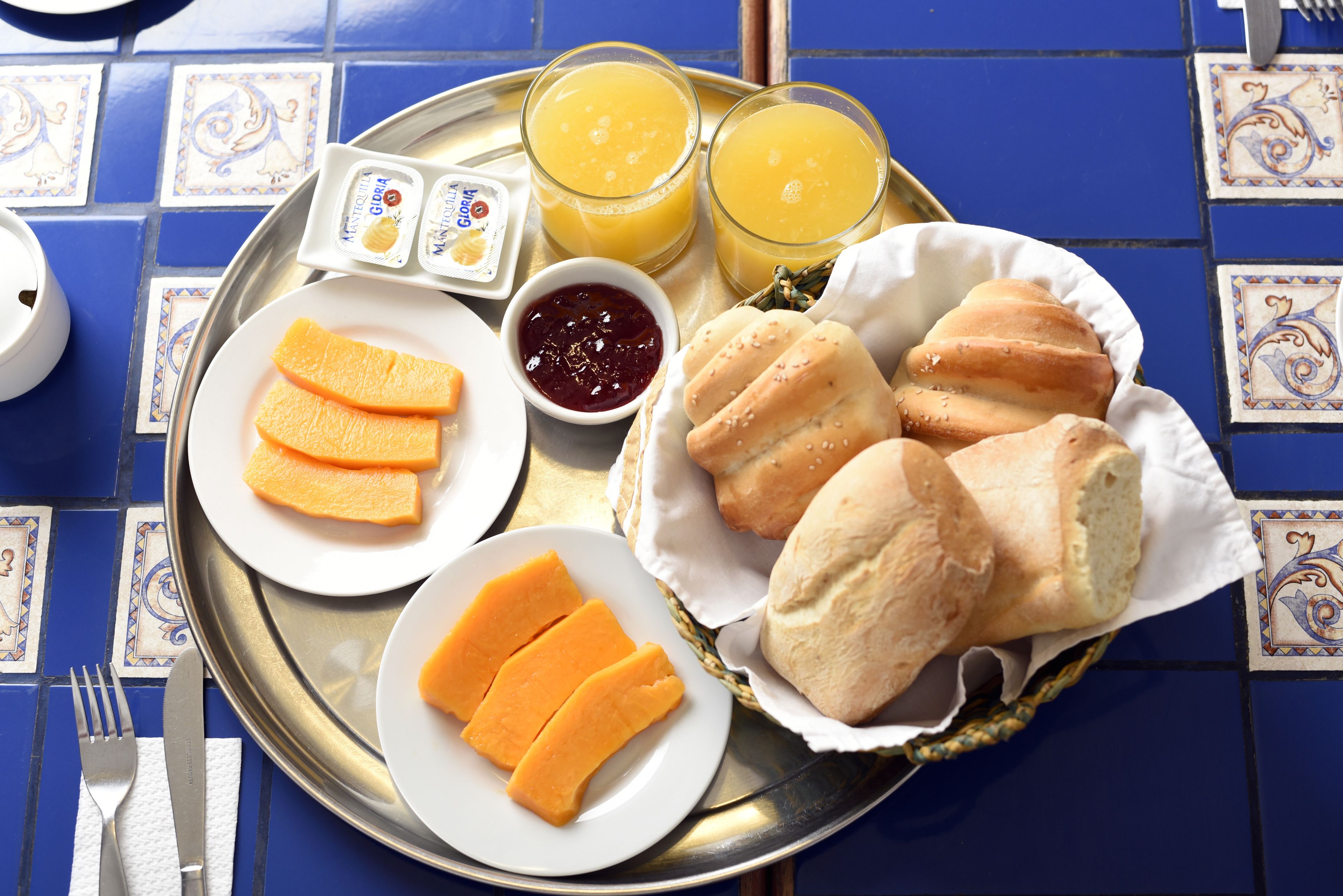 Een dienblad met oranjeslices, brood en twee glazen sinaasappelsap op een betegelde tafel.