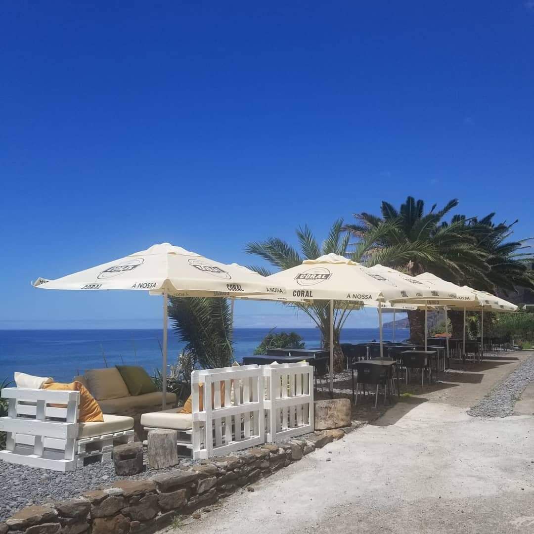 Outdoor seating with umbrellas, a stone wall, and a view of the ocean.