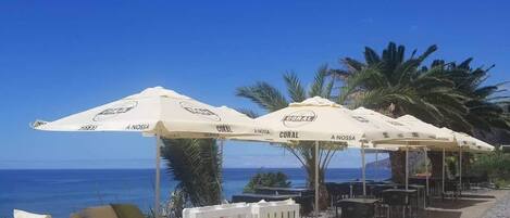 Outdoor seating with umbrellas, a stone wall, and a view of the ocean.