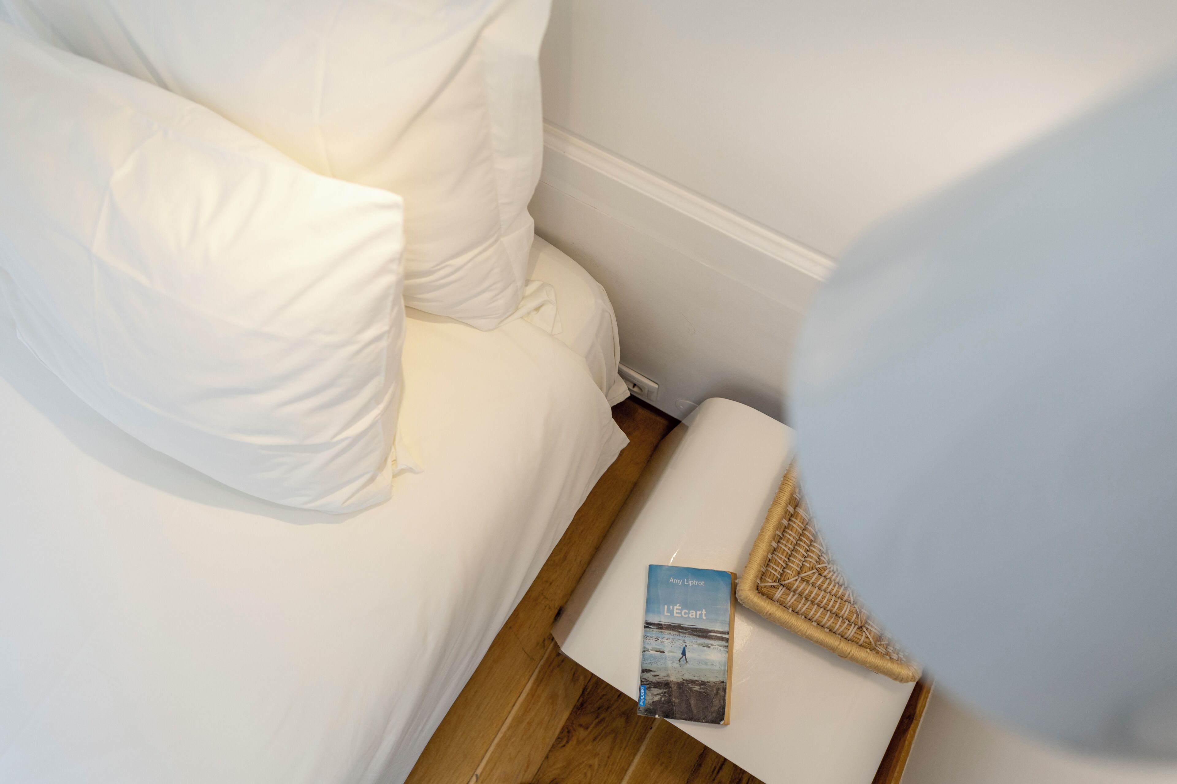 Un canapé blanc, un livre intitulé « L’éart » d’Amy Lighfoot, un panier en osier et un plancher en bois.