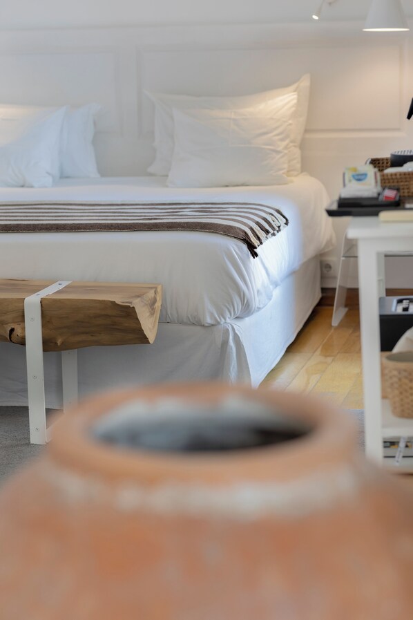 A bed with white bedding, a wooden bench, and a white nightstand with a lamp.