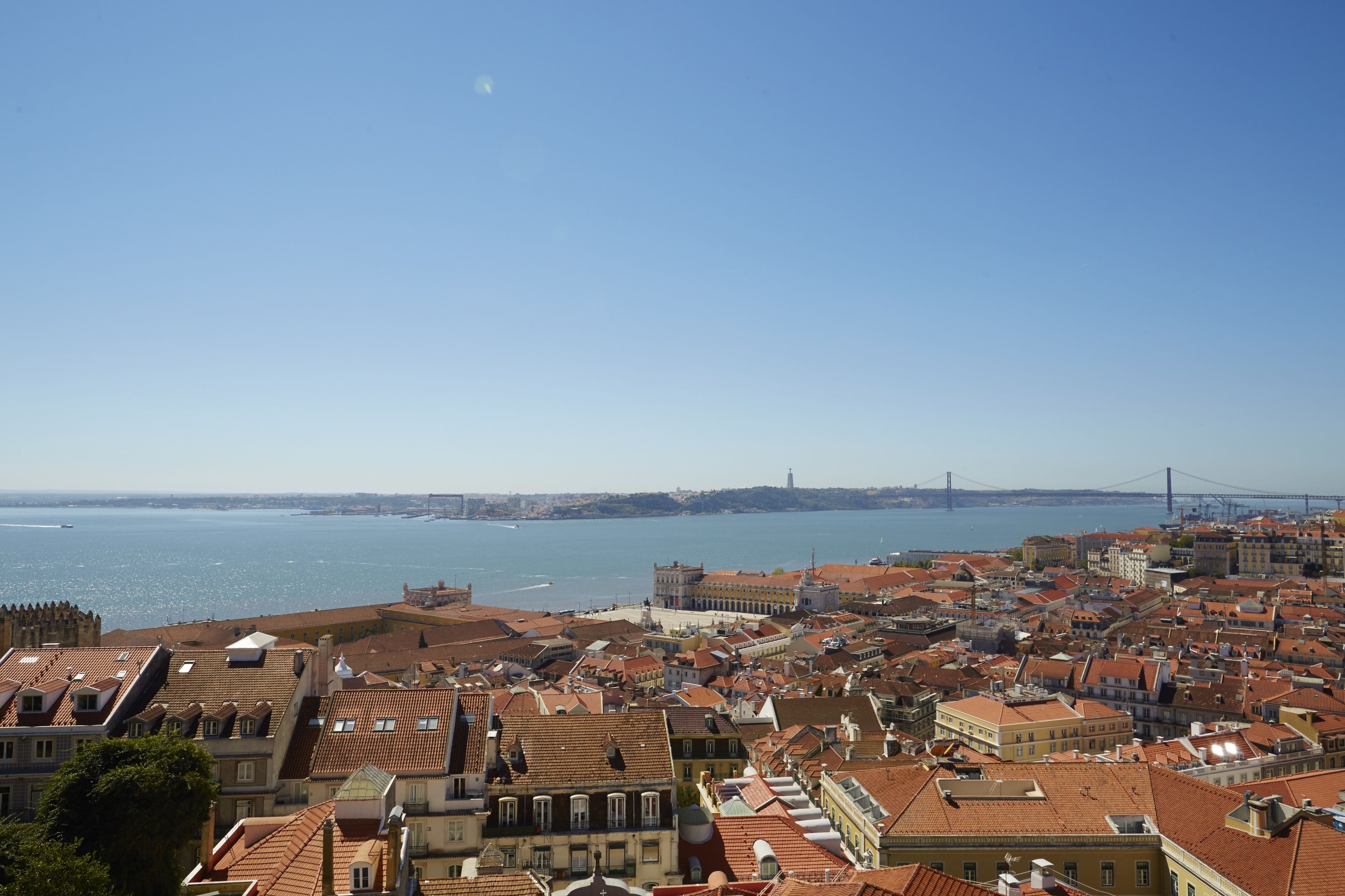 Paisagem costeira urbana com edifícios históricos, uma ponte imponente ao longe e céu claro.