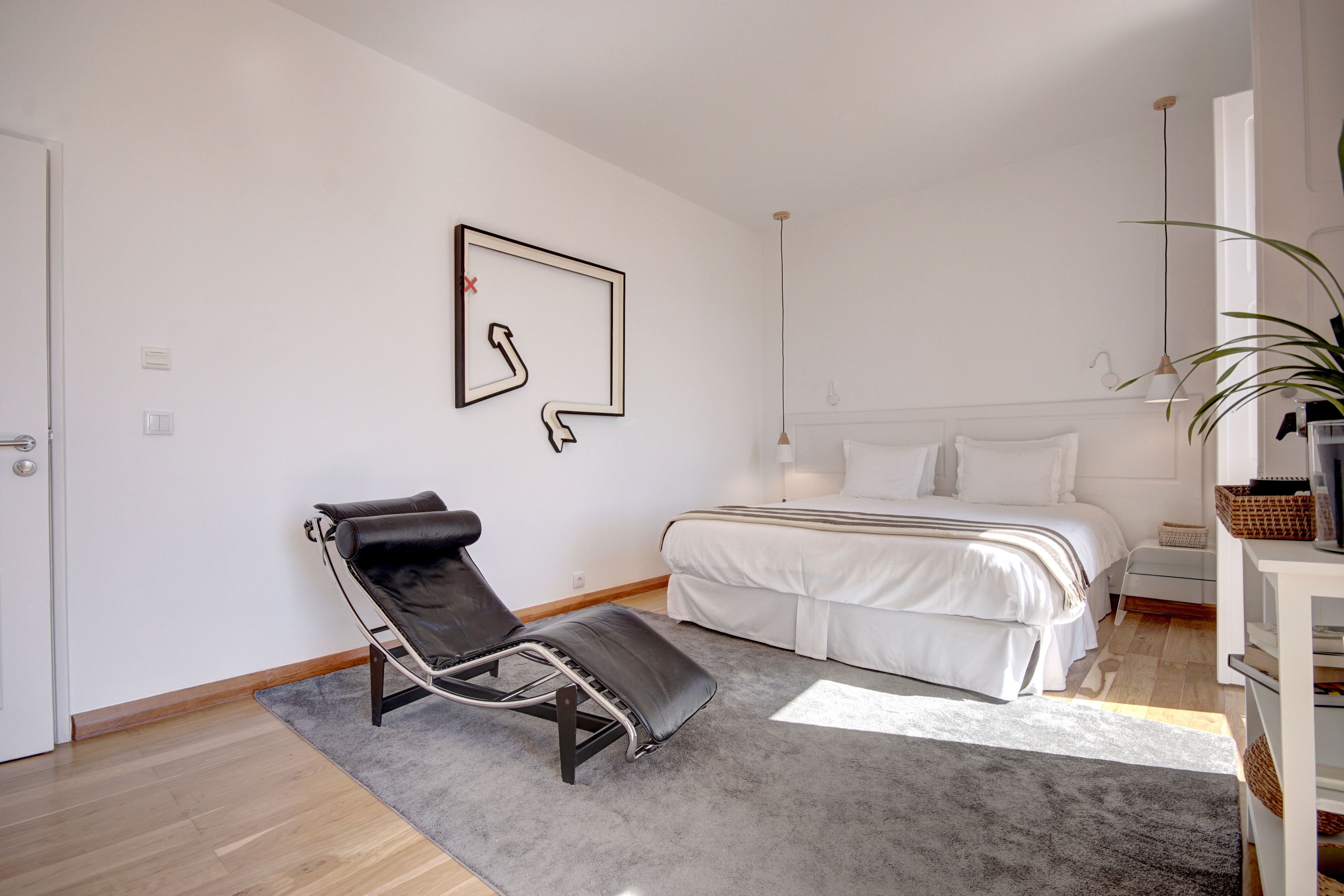 A modern bedroom with a bed, a black lounge chair, a gray rug, and a minimalist wall art piece.