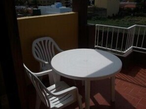 Un pequeño patio exterior con una mesa redonda blanca y dos sillas de plástico blancas.