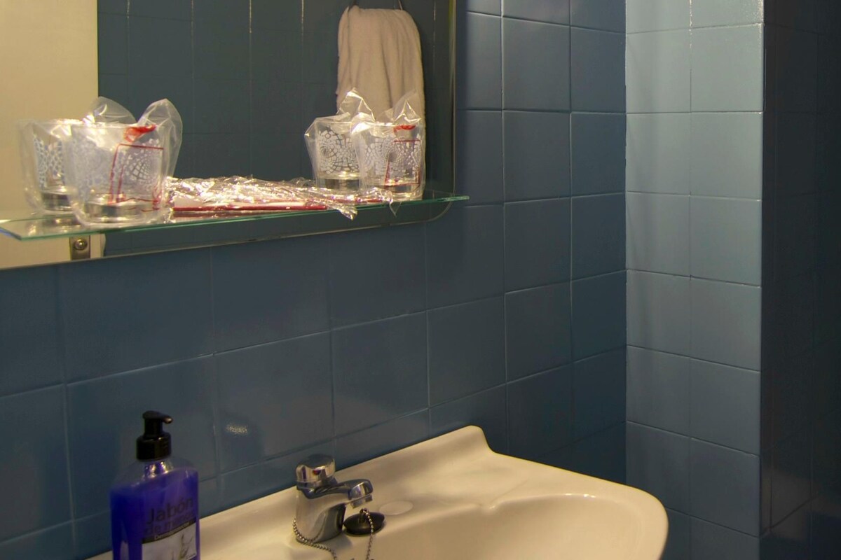 Casa de banho com lavatório branco, espelho e prateleira com produtos de higiene pessoal.